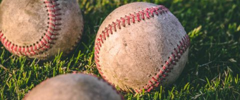 Four old baseballs in the grass.
