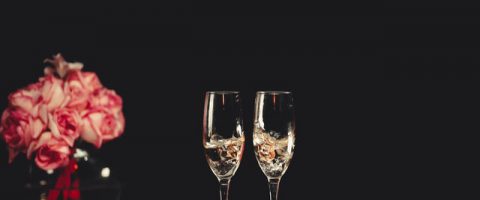 Two champagne flutes next to a pink flower arrangement.