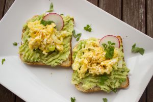 Two slices of bread with egg salad and guacamole on a plate. 