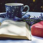 Book of poems open on a table with a teacup and flowers.