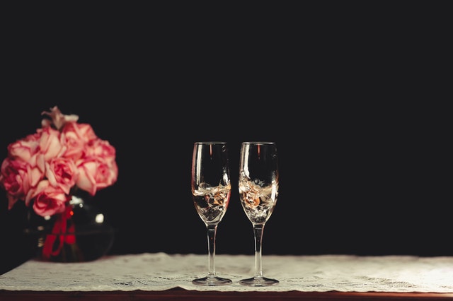 Two champagne flutes next to a pink flower arrangement.