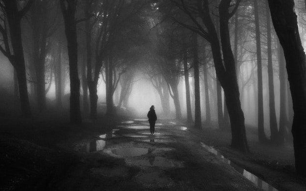 A woman walking alone on a foggy night.