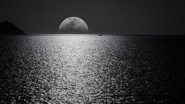 Dark moon peaking over the sea's horizon