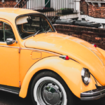 Yellow/orange vintage VW Beetle parked outside a brick building