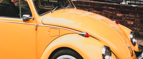 Yellow/orange vintage VW Beetle parked outside a brick building