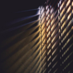 sunlight creeps through venetian blinds into a dark room