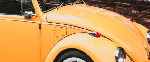 Yellow/orange vintage VW Beetle parked outside a brick building