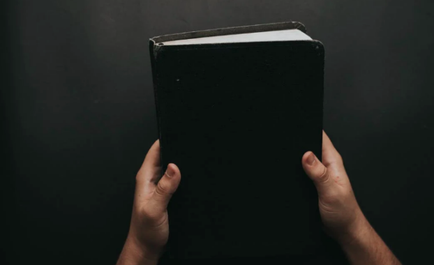 A pair of hands hold up a black book.