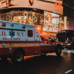 An ambulance driving through a city at dusk.