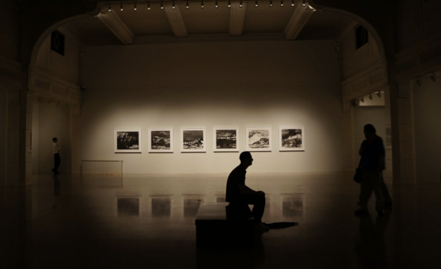 A silhouetted figure sits on a bench in an art gallery.