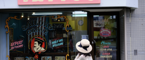 A woman in a sun hat facing a tattoo parlor's colorfully decorated storefront