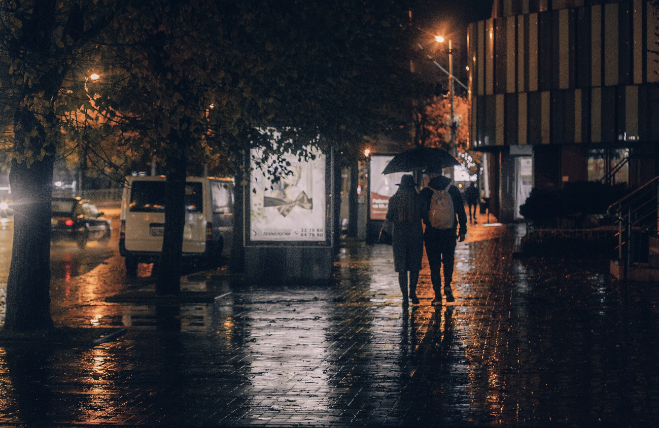 A couple walking through the city streets at night, under an umbrella in the rain