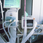 The edge of a hospital bed surrounded by tubes, wires and screens