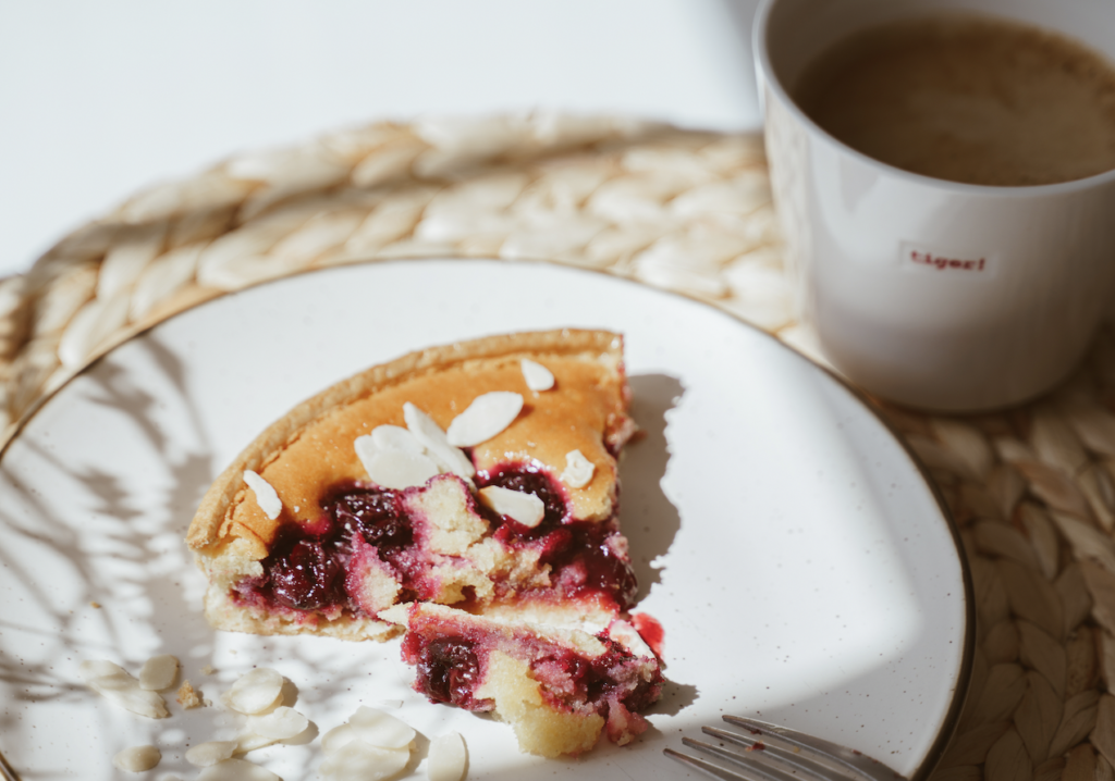A piece of cherry pie on a plate next to a cup of coffee