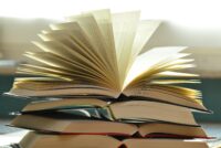 An open book stacked onto other books.
