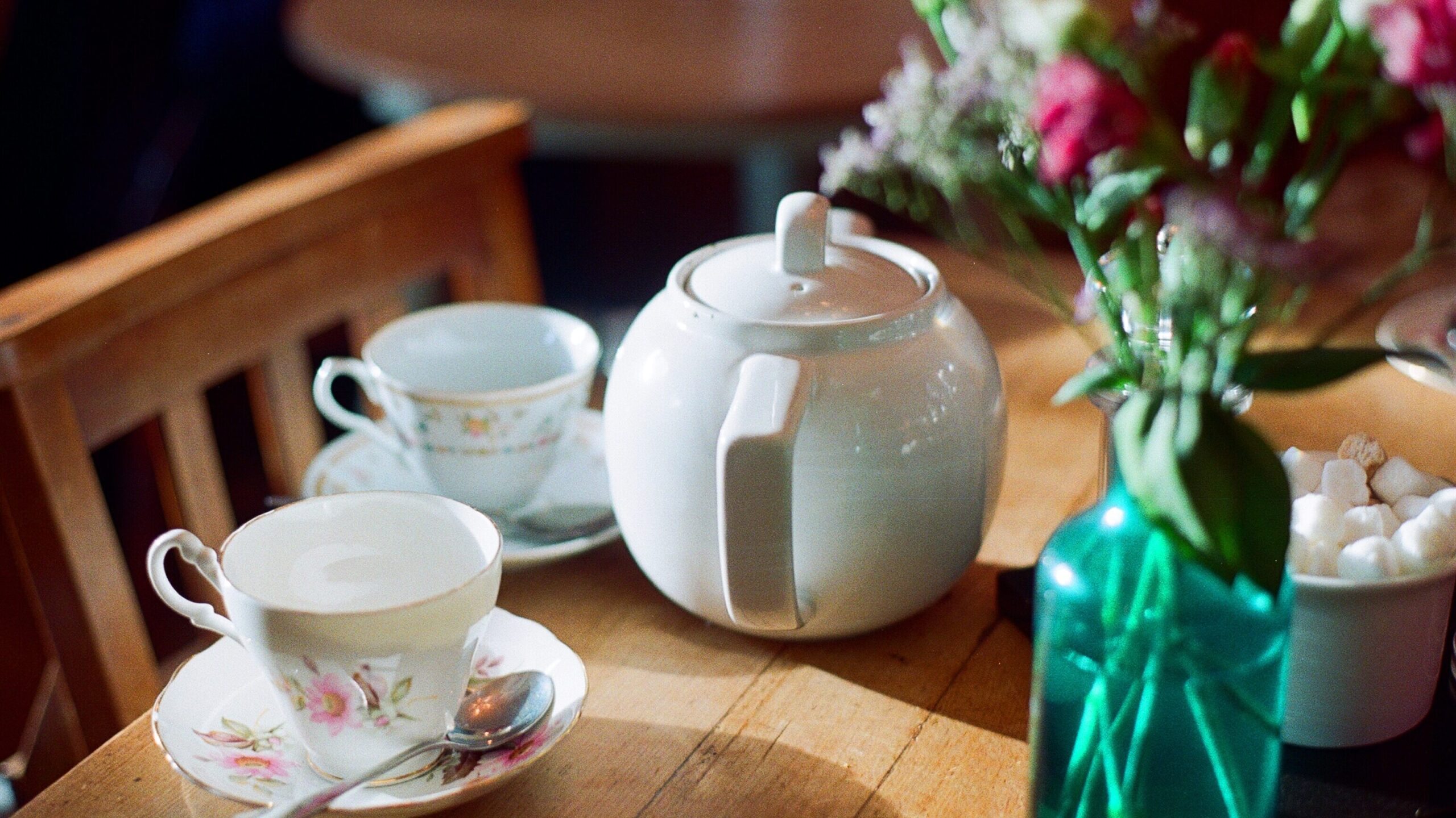 Teapot beside two teacups and a vase of flowers