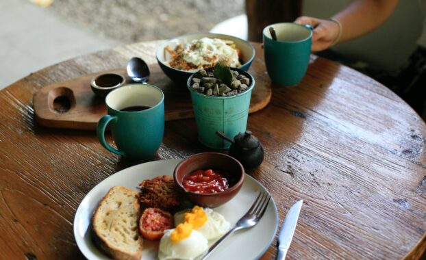 Person holding a mug sitting at a table with a plate of breakfast